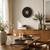 Horloge murale sur un mur : motif rond noir, cadran en bois, cadre clair