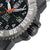 Détail de montre homme : boîtier cannelé avec pointe d'aiguille orange et protection latérale contre les pliures.
