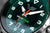 Nahaufnahme Herrenuhr: grünes Zifferblatt mit Leuchtindizes, Metallzeigern und Datumsangabe