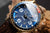 Montre homme en détail : cadran bleu avec aiguilles lumineuses, boîtier doré