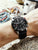 Herrenarmbanduhr am Handgelenk: schwarzes Lederband, schwarzes Chronograph-Zifferblatt
