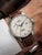 Herrenuhr am Handgelenk mit braunem Lederarmband, hellem Zifferblatt und Datumsfenster