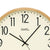 Cadran de montre murale en détail : fond beige, chiffres 12 et aiguilles noirs, bordure en bois clair.