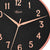 Gros plan d'une horloge murale : cadran noir, aiguilles or rose et chiffres romains